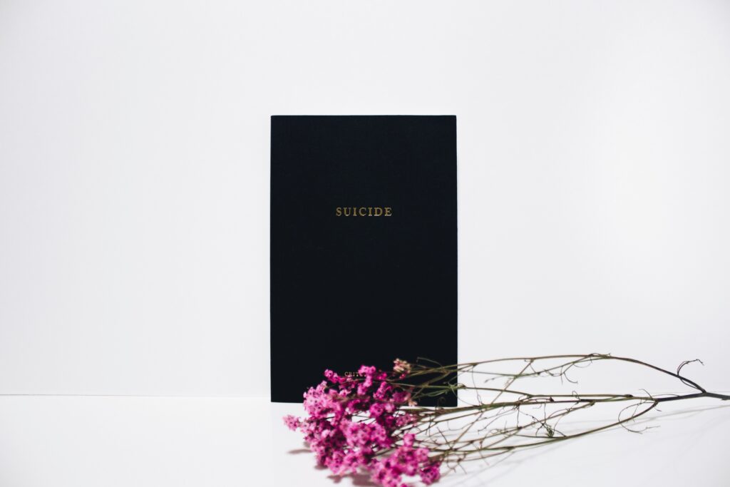 Ein schwarzes Buch mit der Aufschrift „Suicide“ und davor liegenden Blumen